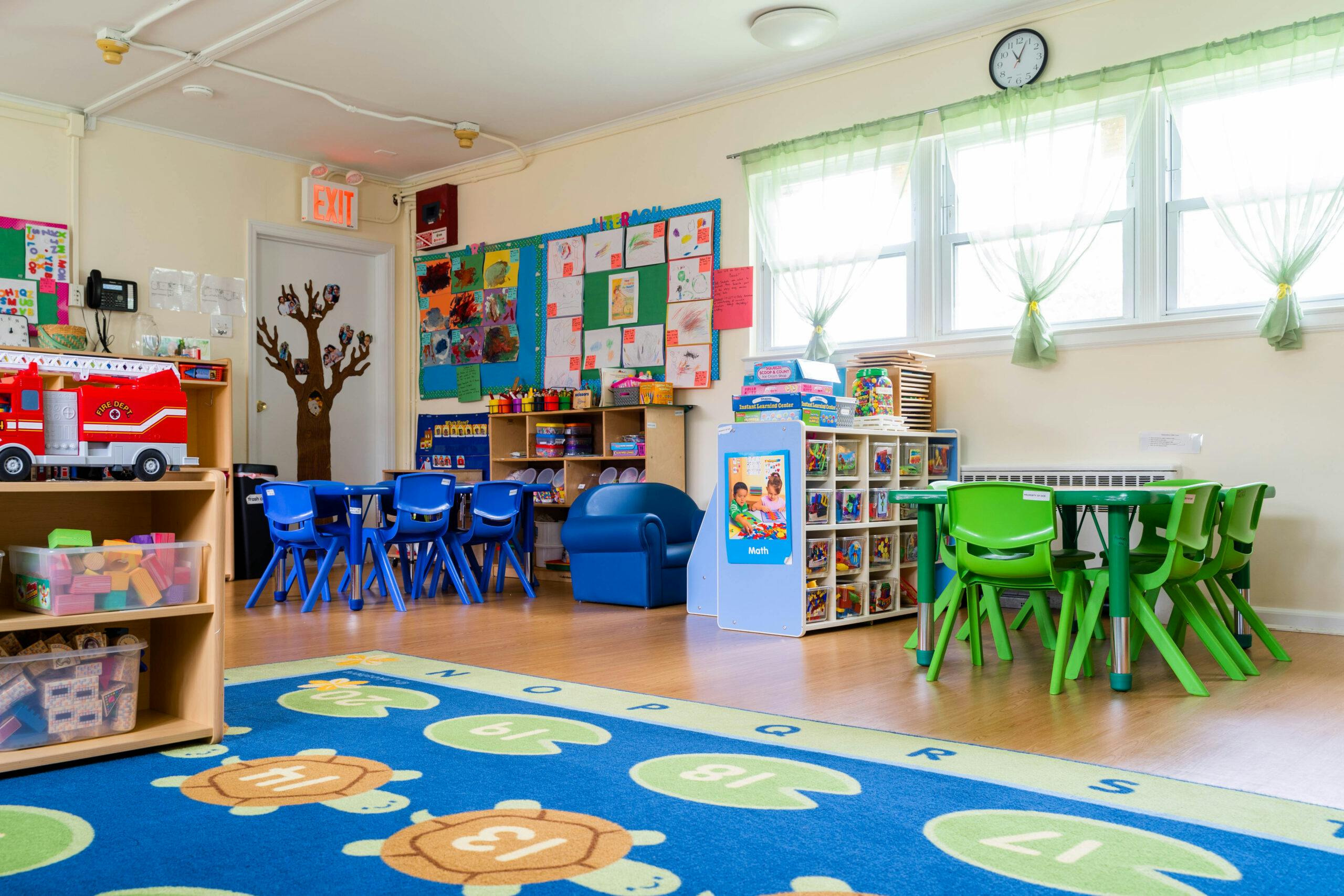 Children's classroom with small tables and chairs, shelves of toys, and colorful rug
