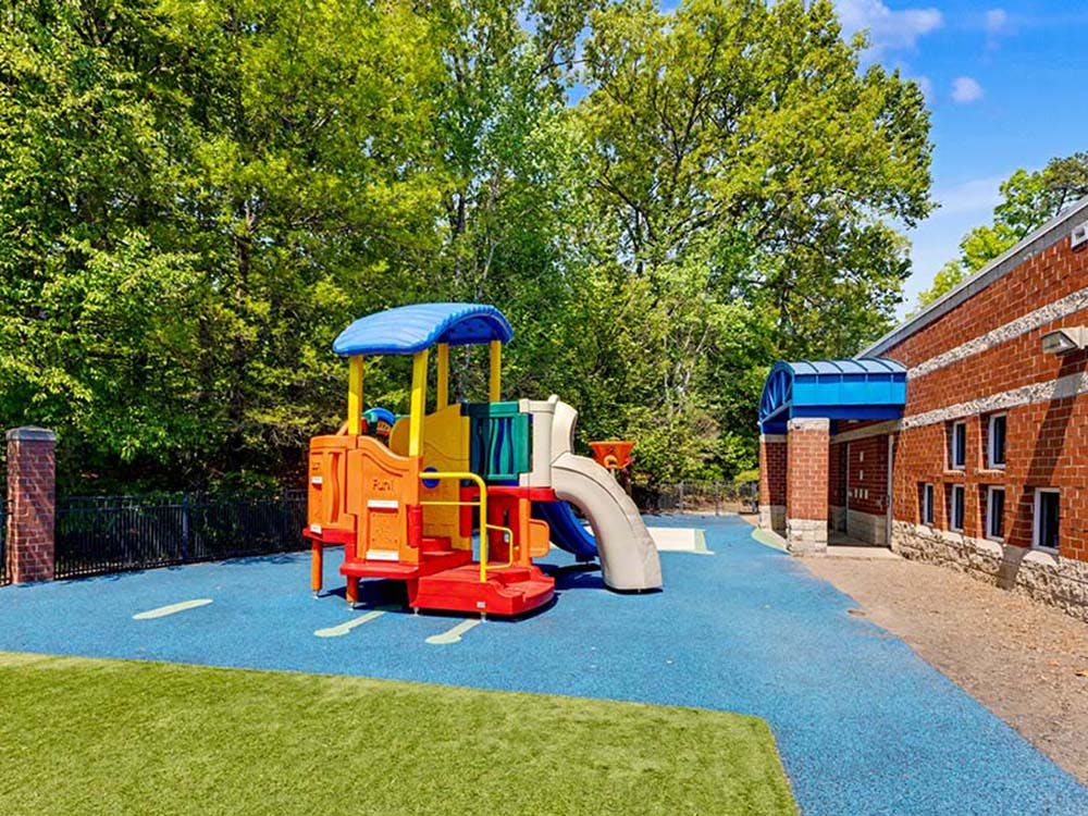 Colorful playground structure on blue soft surfacing next to a brick building