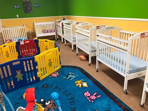 Multiple cribs in a room with a playpen and a colorful rug