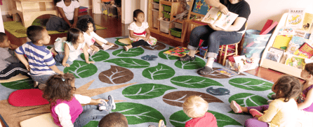 Adult reading a book to children sitting on a leaf-patterned rug