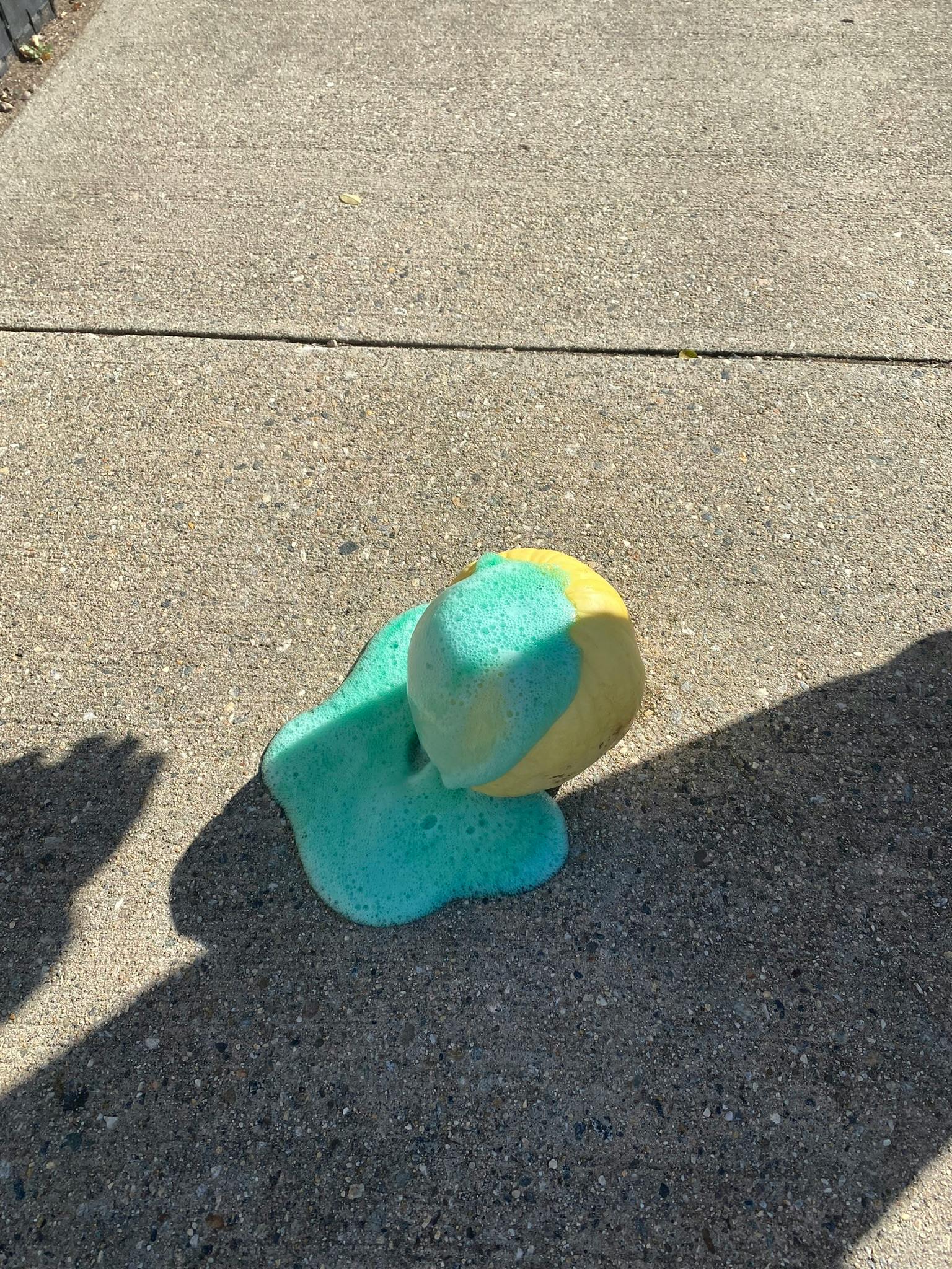 Yellow and blue ball on a puddle of blue liquid on concrete