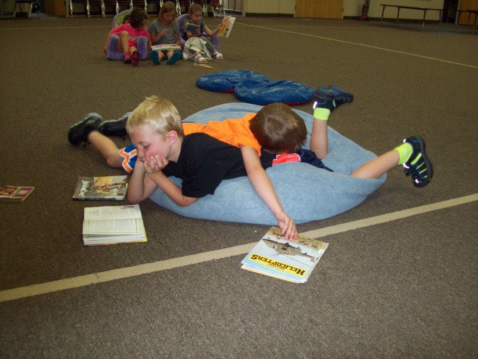 Two children lying on a beanbag chair reading books