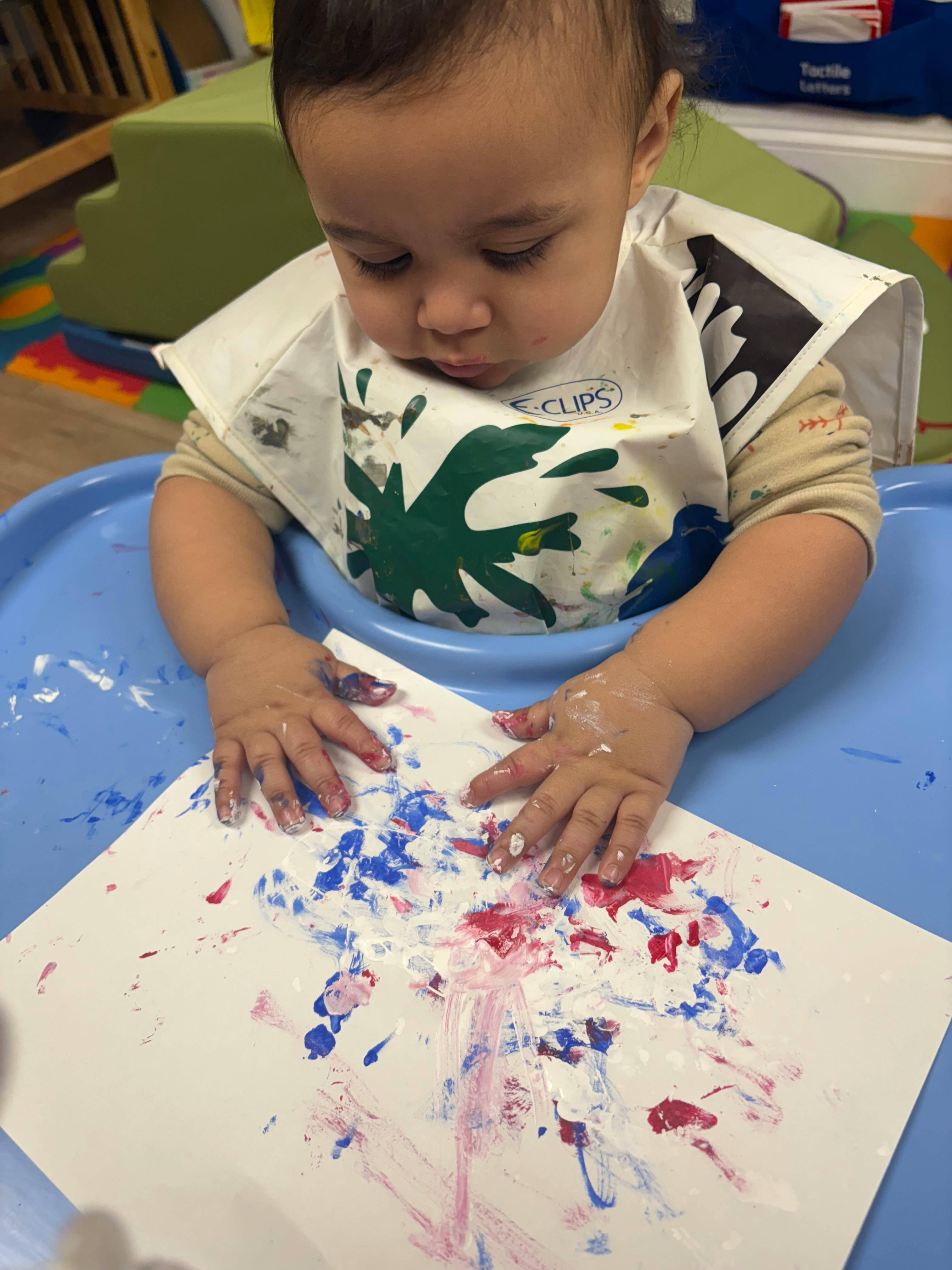 Child in a high chair finger painting with red and blue paint on paper