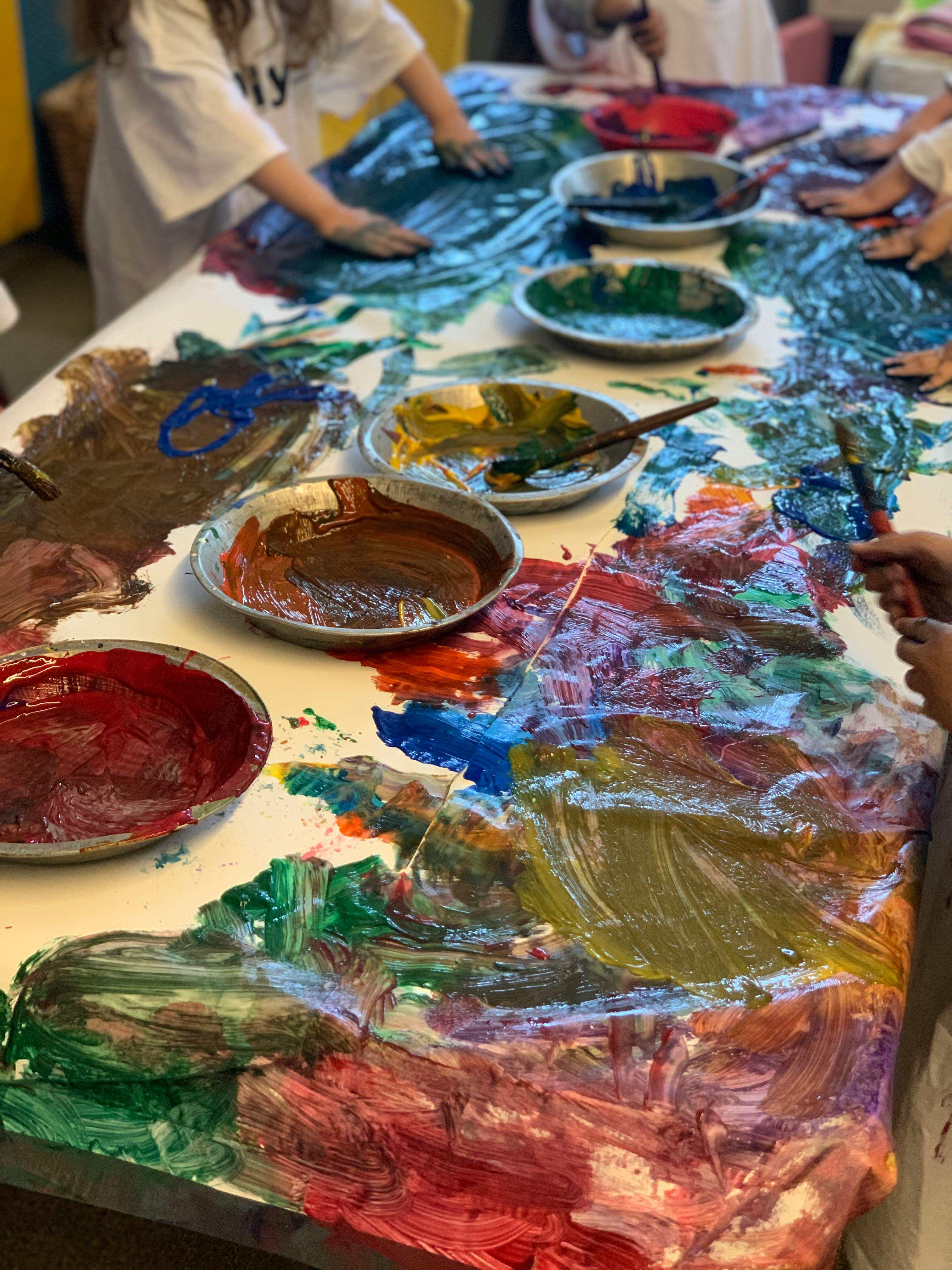 Children finger painting on a table covered in colorful paint
