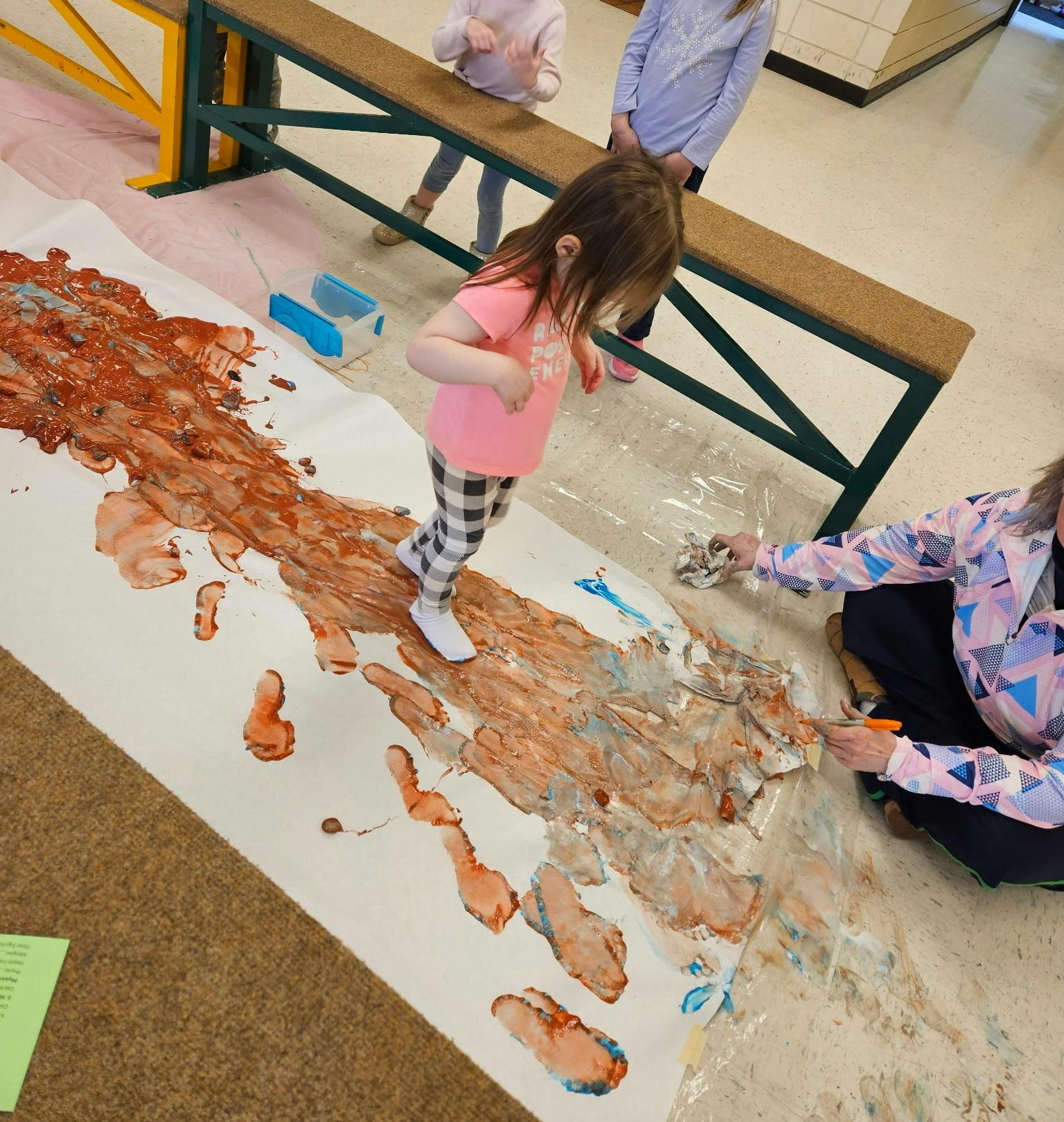 Child stepping on a large sheet of paper covered in brown and blue paint