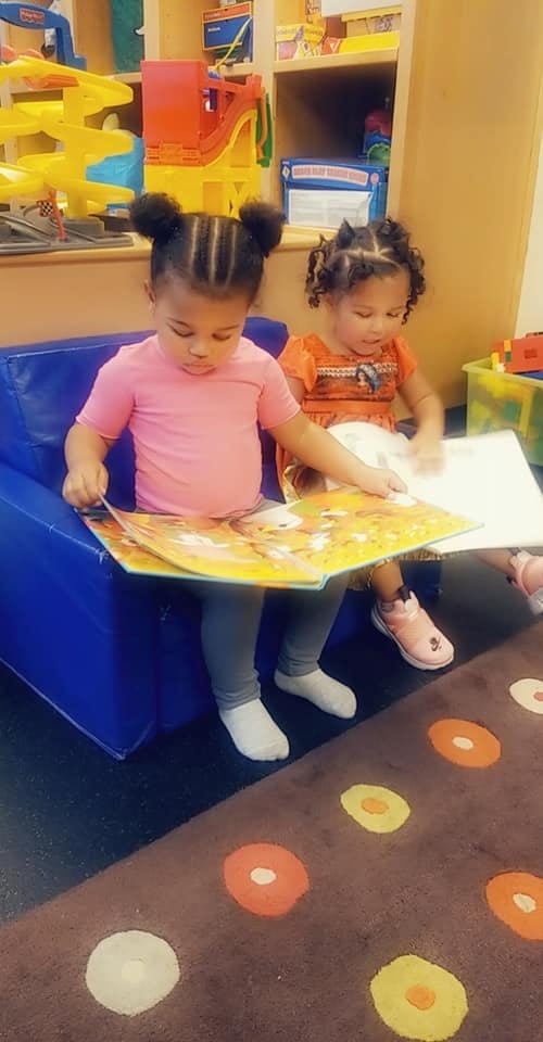 Two children sitting on a blue chair reading a book