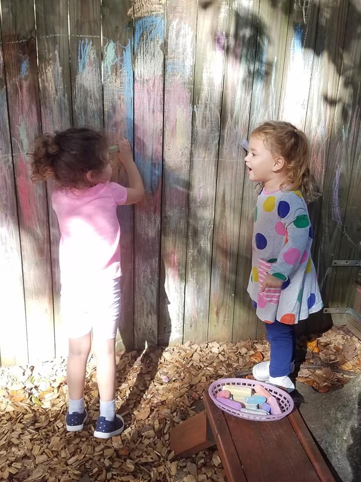 Two children playing with chalk on a wooden fence