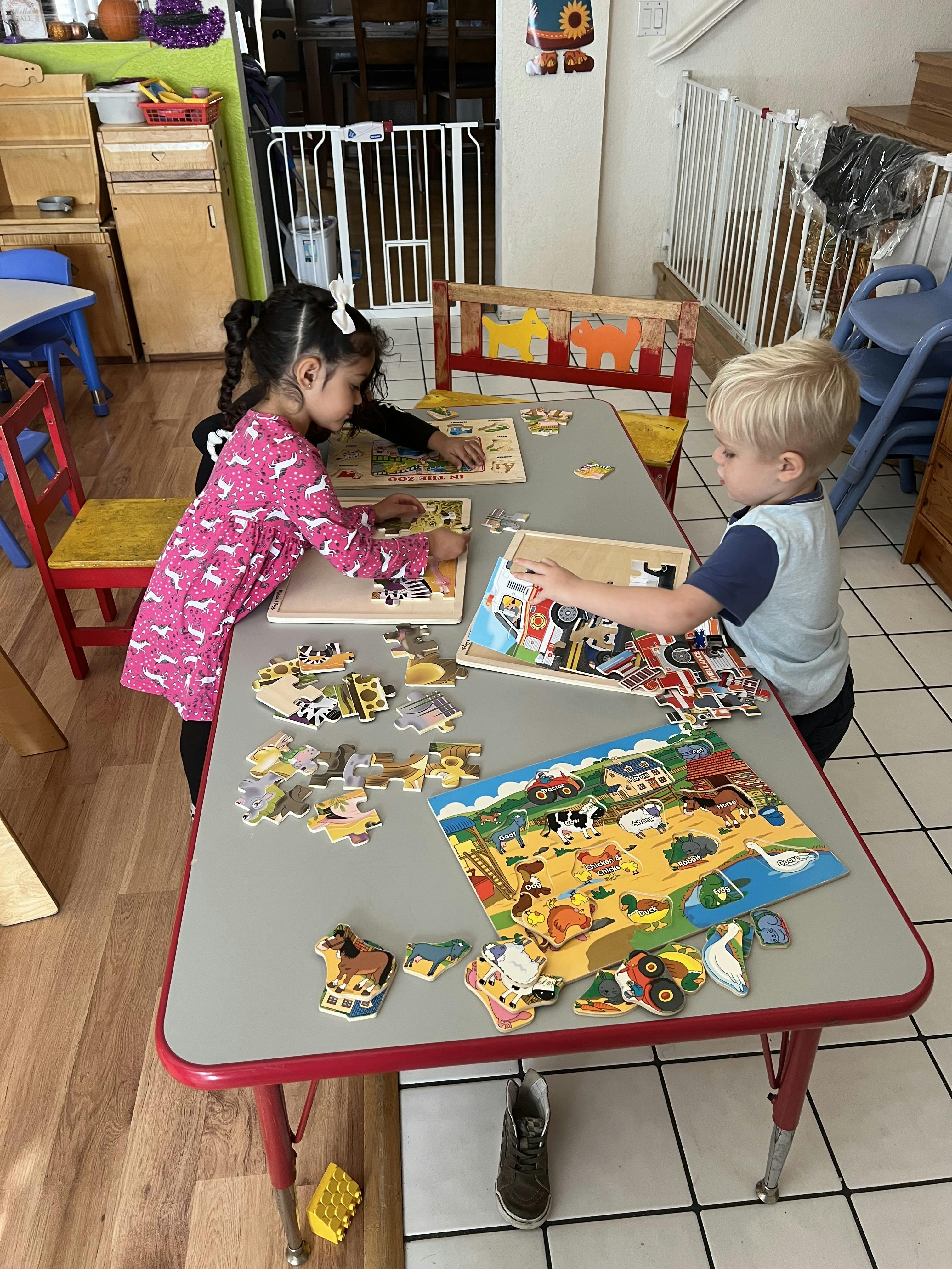 Child and toddler playing with puzzles at a table in a classroom