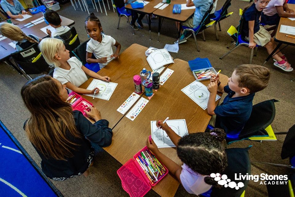 Adult and children seated at a table, writing and drawing