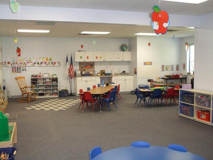 Classroom with small tables and chairs, storage shelves, and a kitchen area