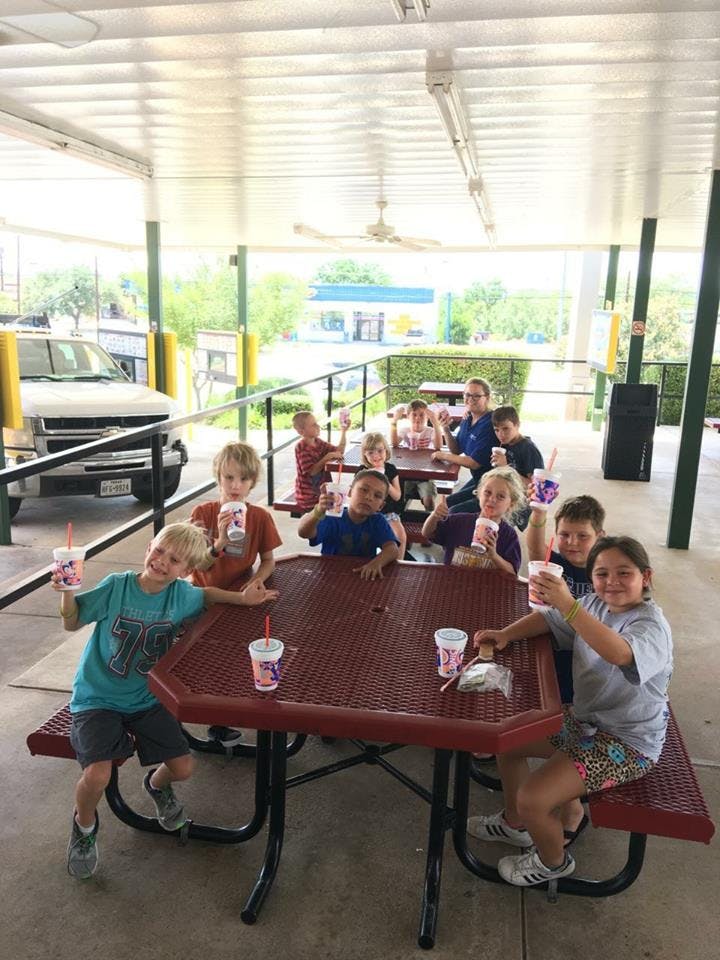 Group of children and adults sitting at picnic tables with drinks