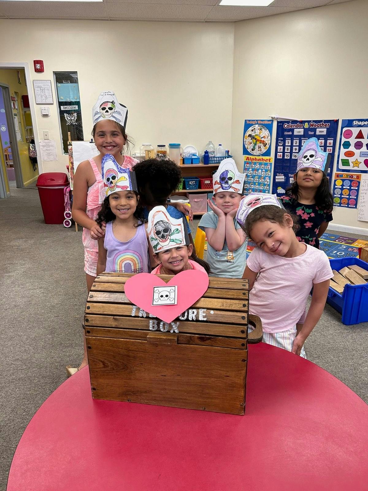 Children wearing paper hats with a wooden box and heart-shaped box