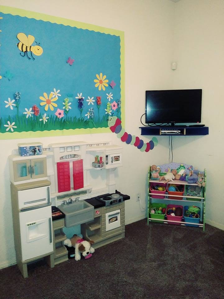 Play kitchen set with a stuffed animal on the floor, a TV, and a bulletin board