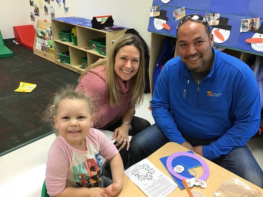 Two adults and a child smiling at a table in a classroom