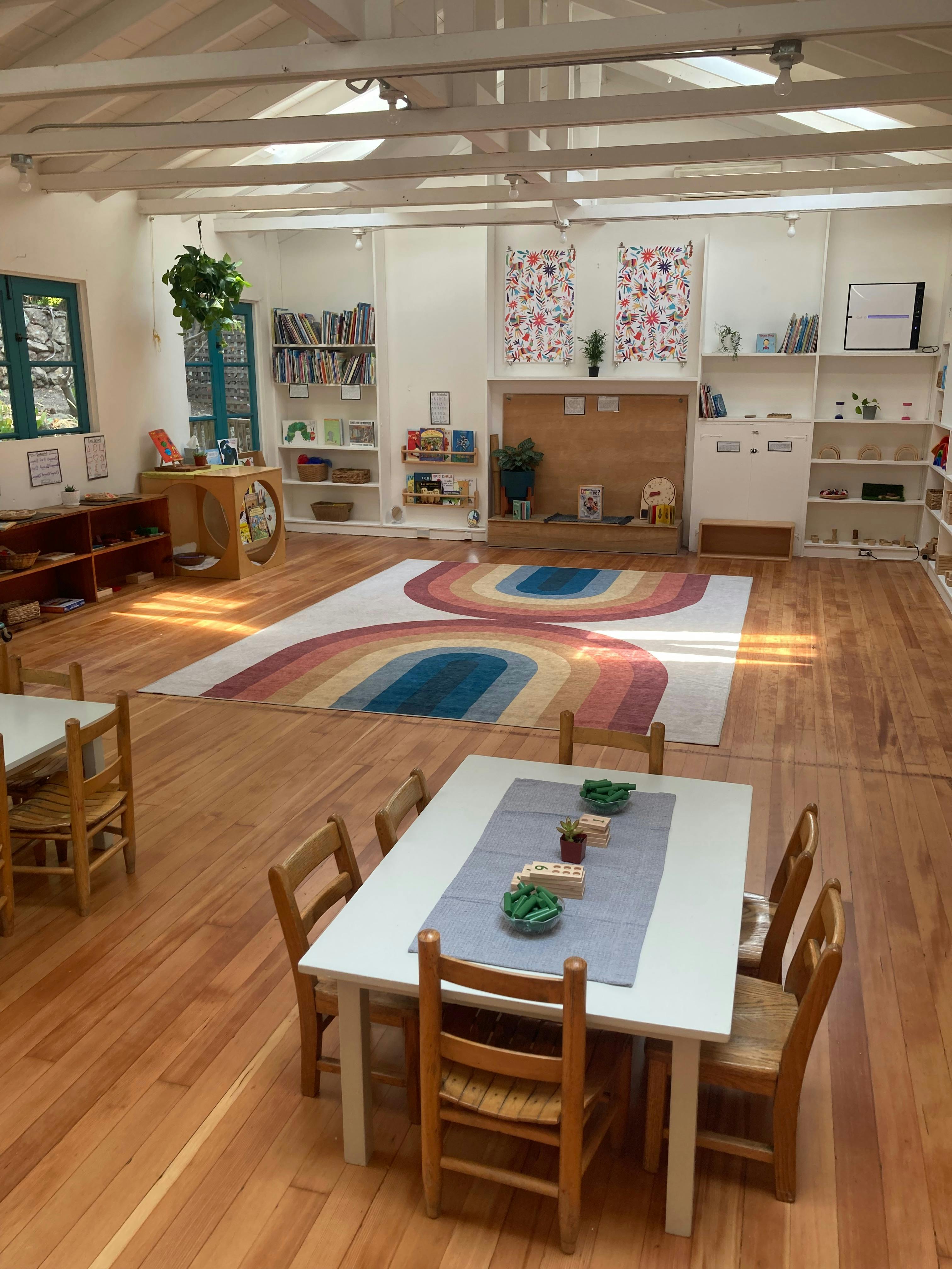 Classroom with tables and chairs, bookshelves, and a rainbow rug