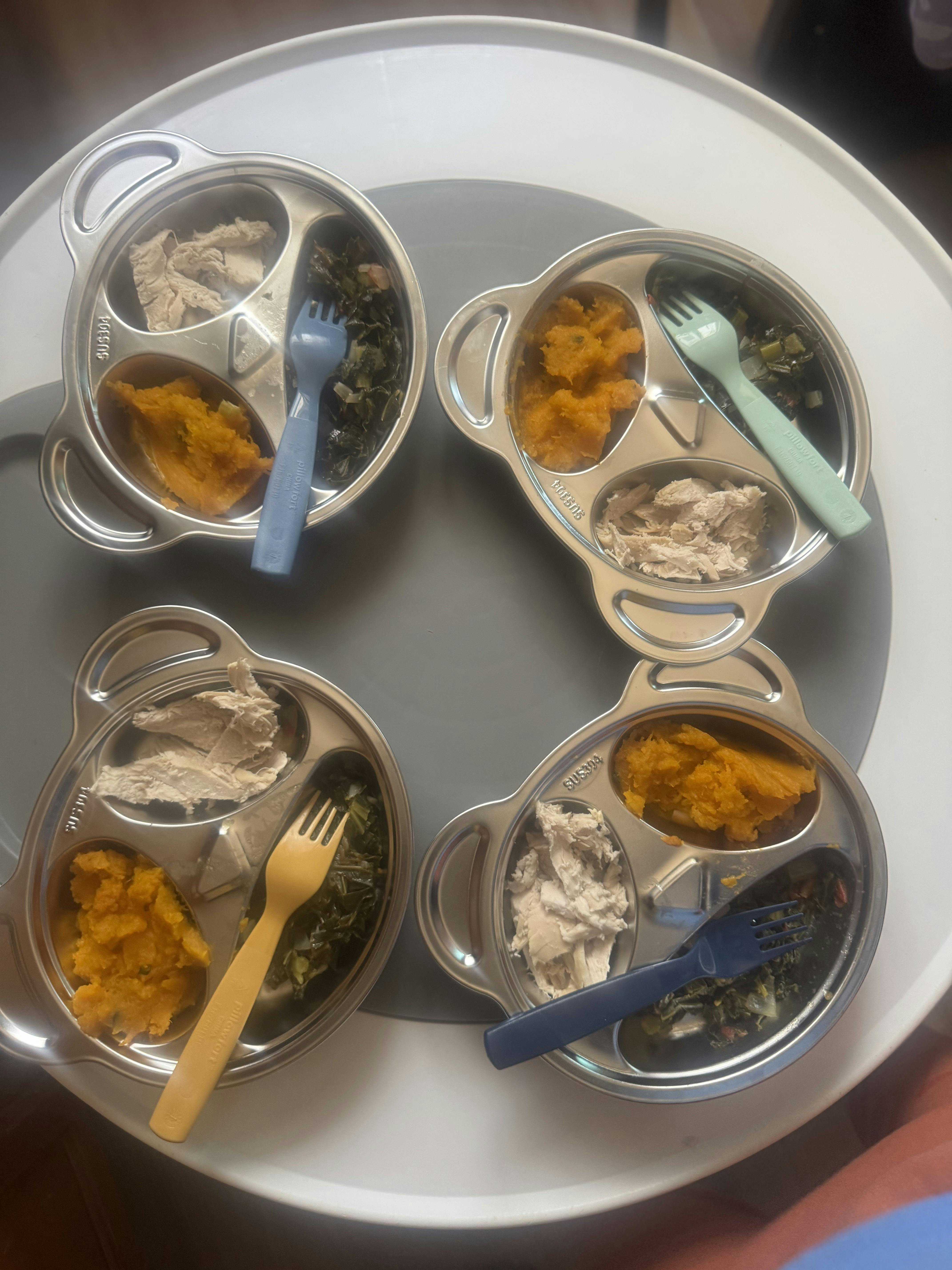 Four divided stainless steel plates with servings of shredded meat and vegetables
