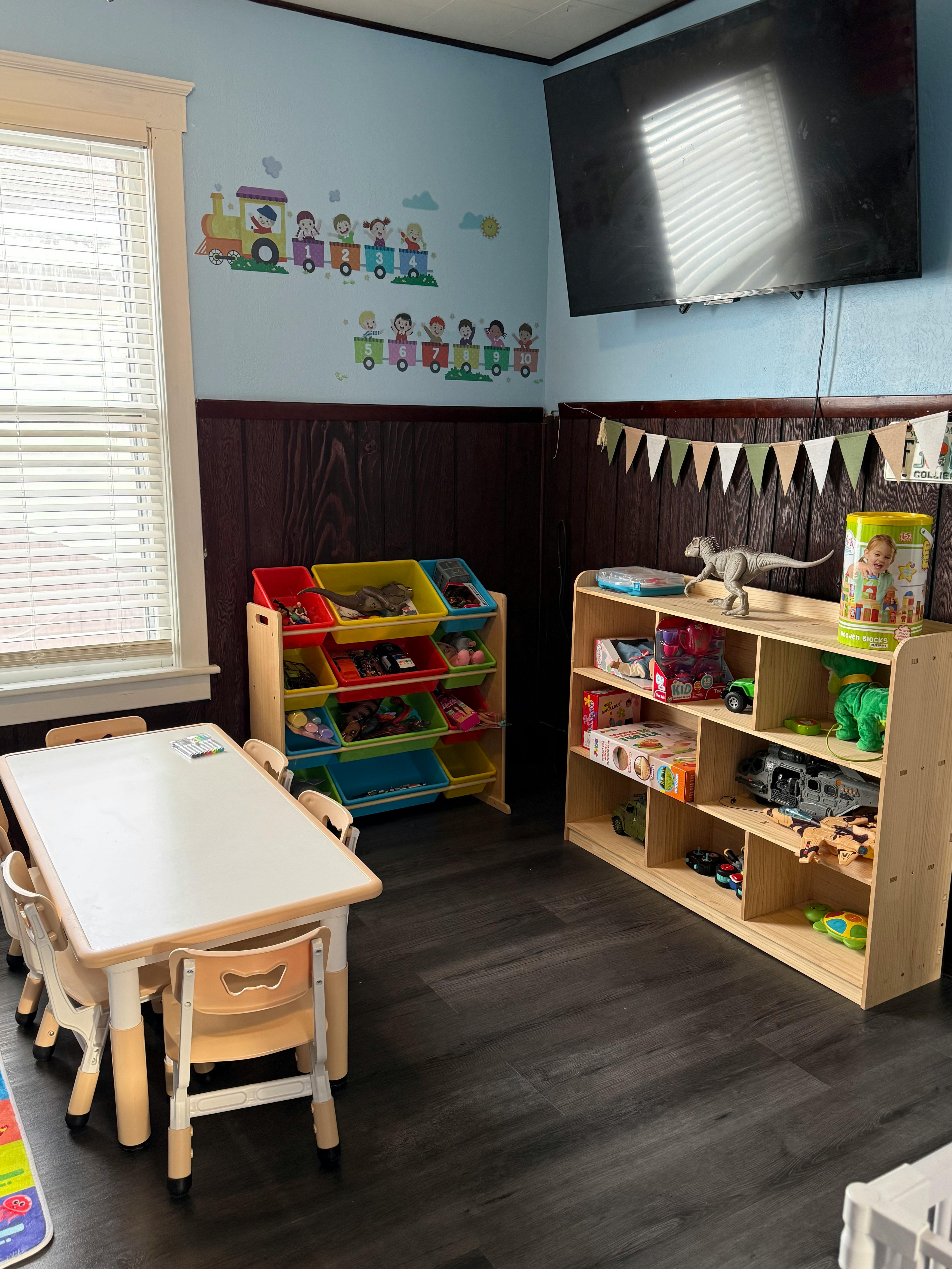 Children's play area with small table and chairs, toy storage, and wall decor