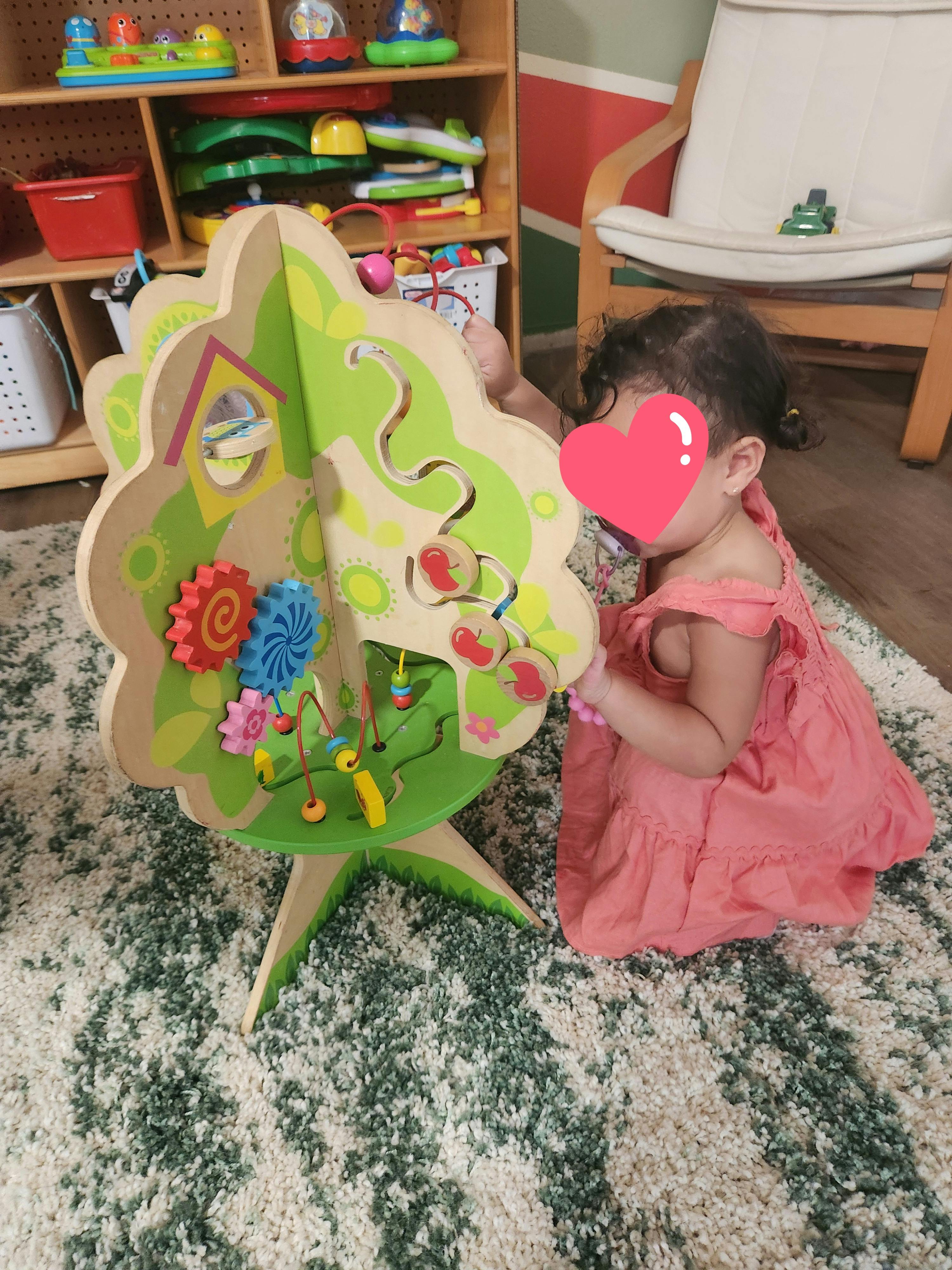 Child playing with a large wooden activity center shaped like a tree