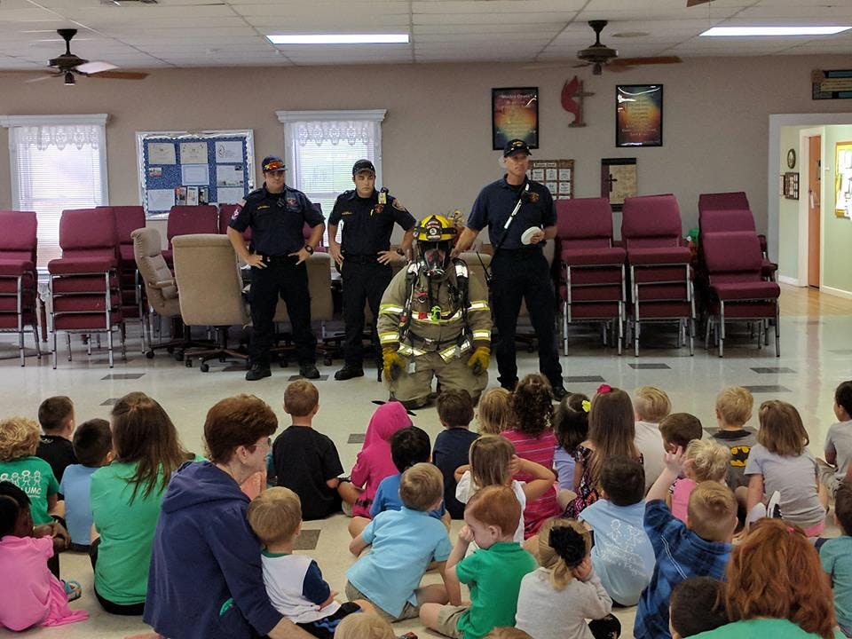 Firefighter in full gear kneeling in front of children and adults
