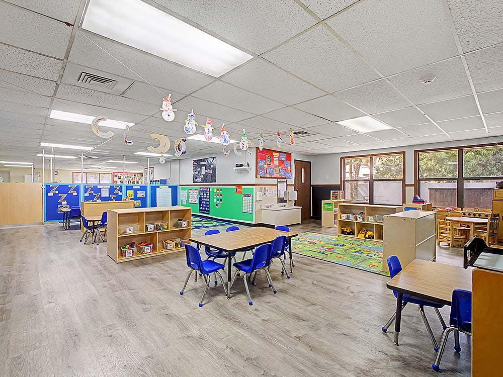 An empty classroom with small tables and chairs, shelves, and decorations
