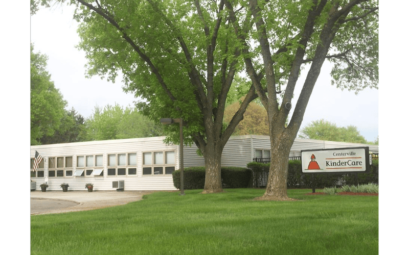 White building with many windows, Centerville KinderCare sign, and trees