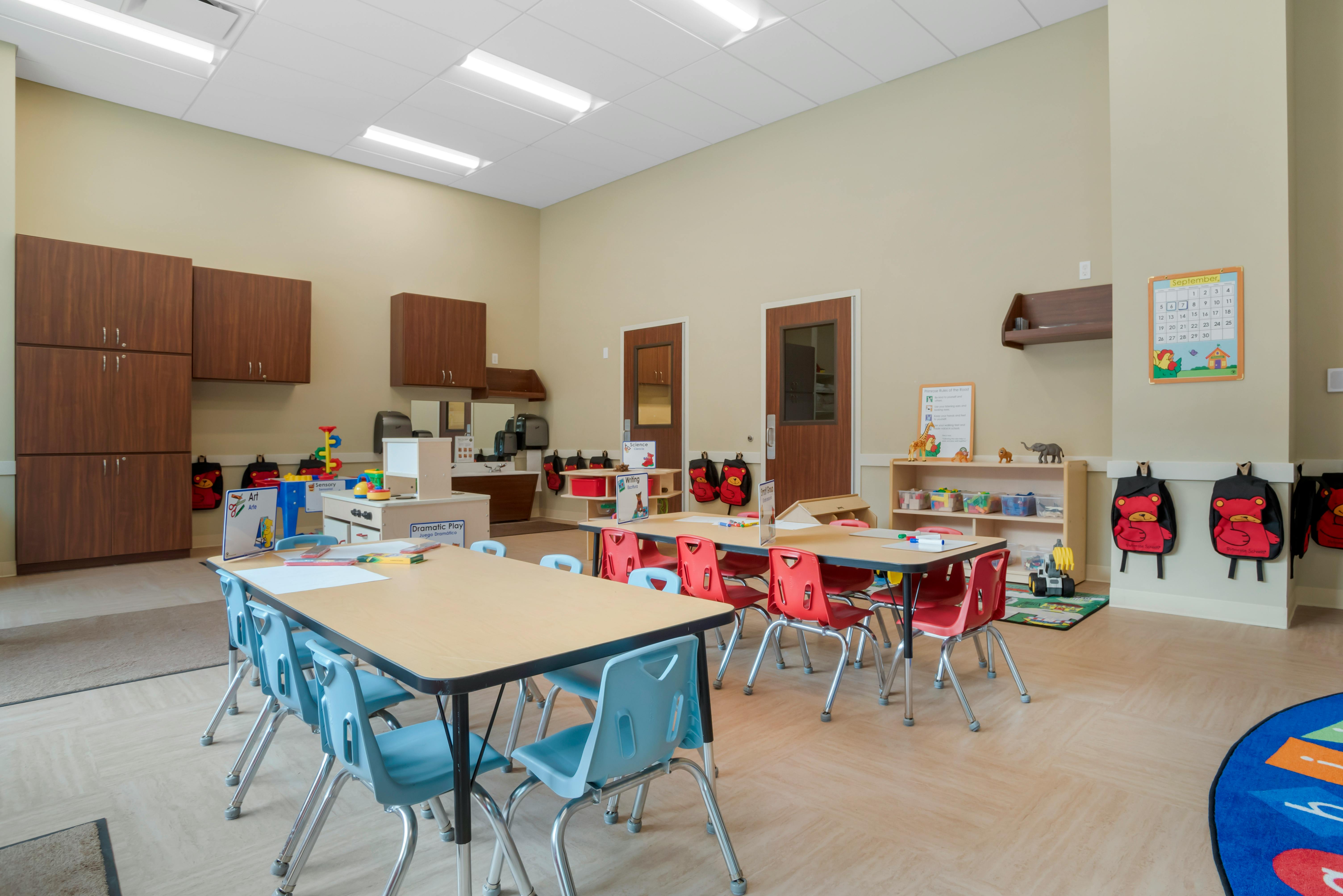 Classroom with child-sized tables and chairs, play areas, and storage cabinets