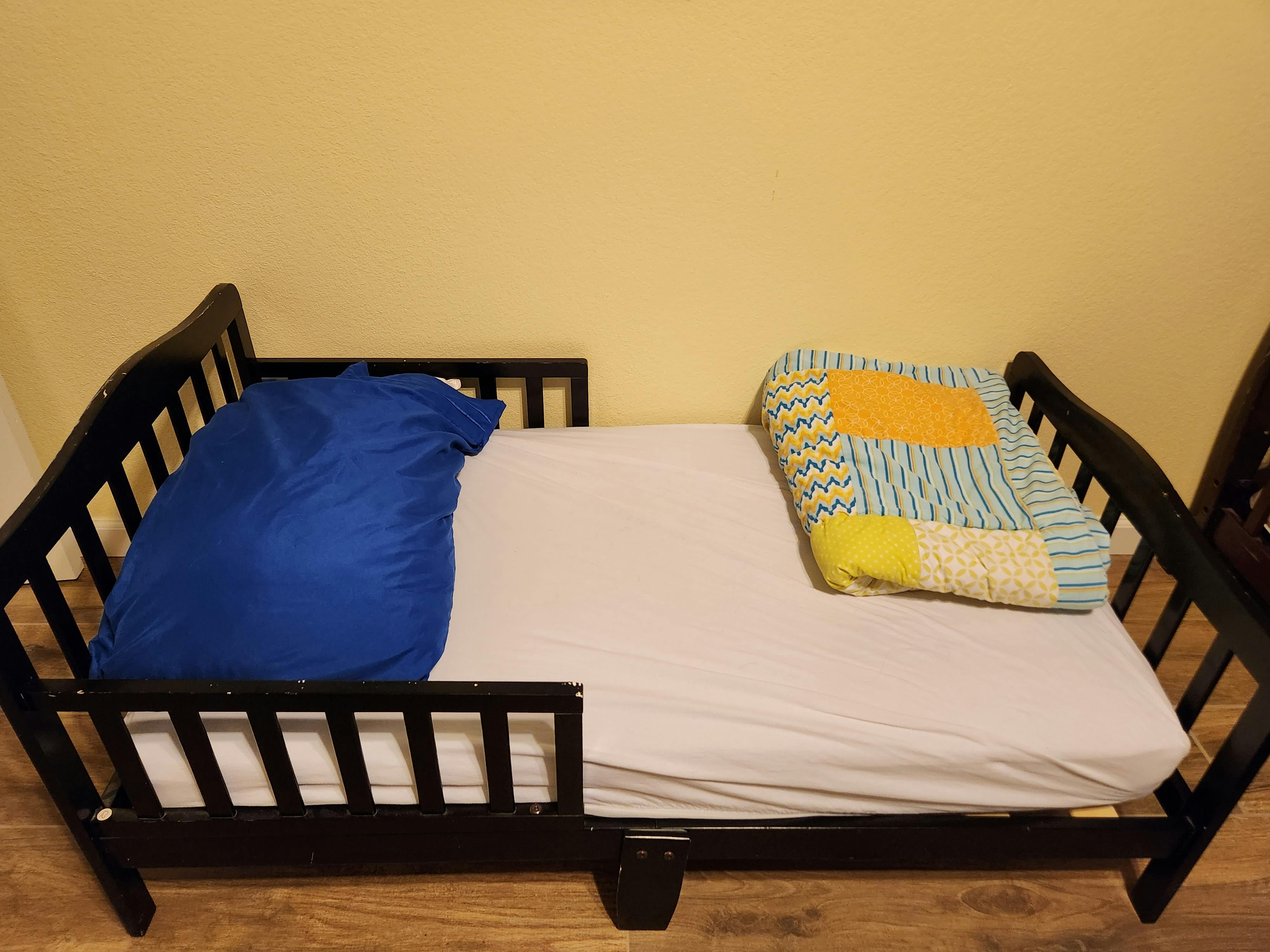 Toddler bed with blue pillow and colorful blanket