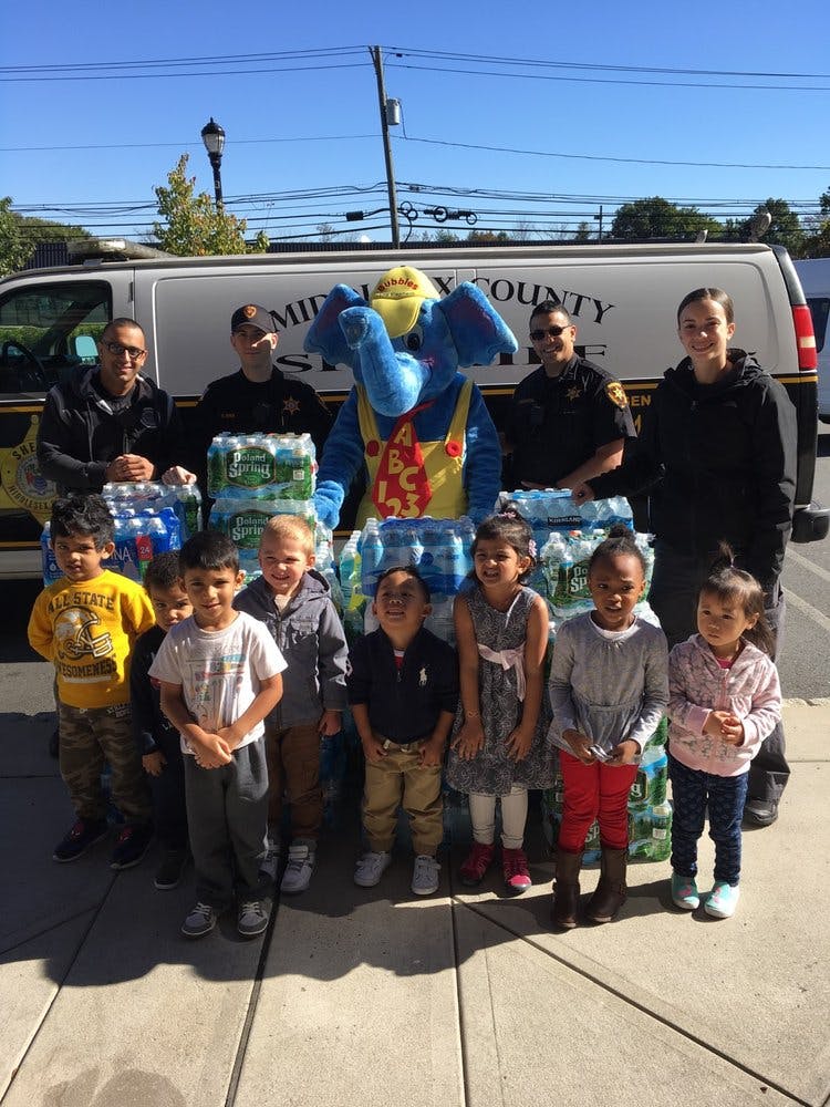 People and children with a mascot and cases of bottled water