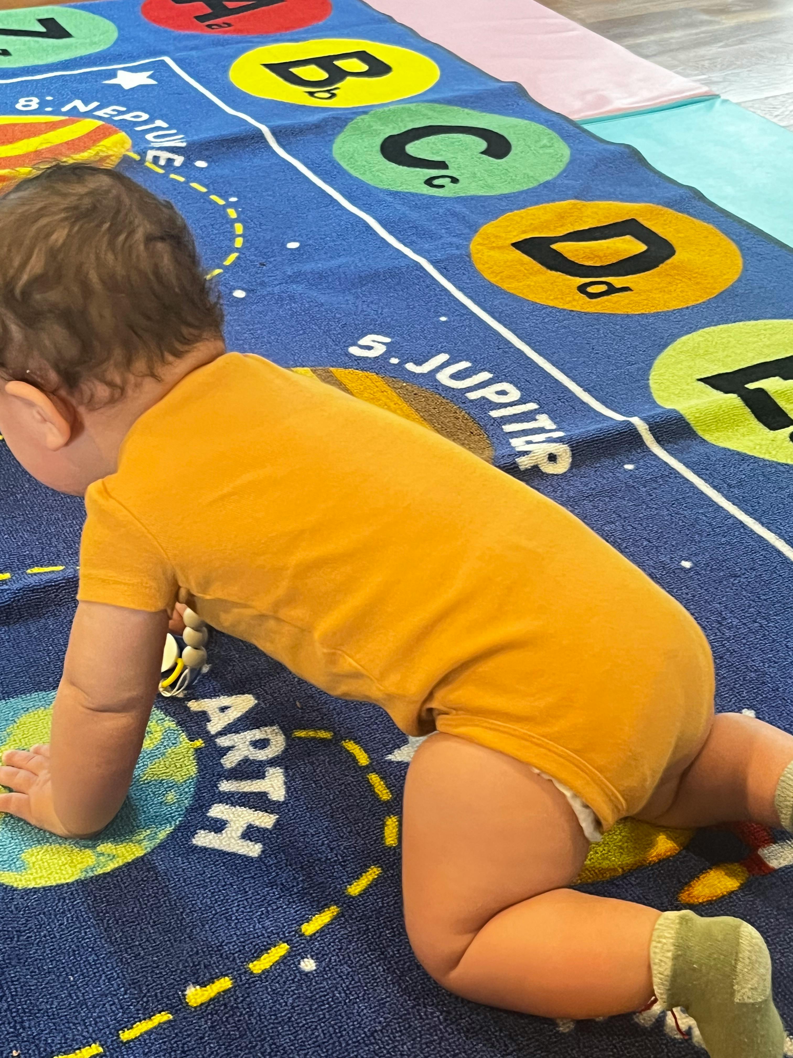 Child crawling on a blue mat with letters and planets