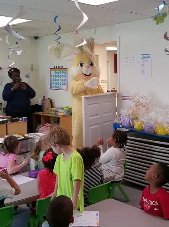 Person in bunny costume holding a door in a classroom with children