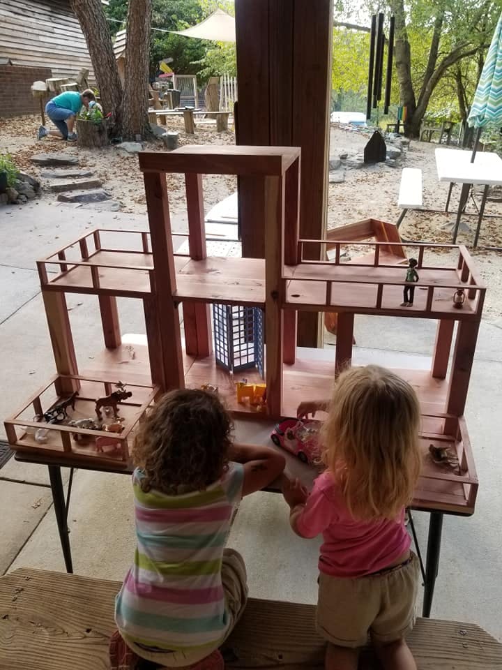 Two children playing with a wooden dollhouse outdoors