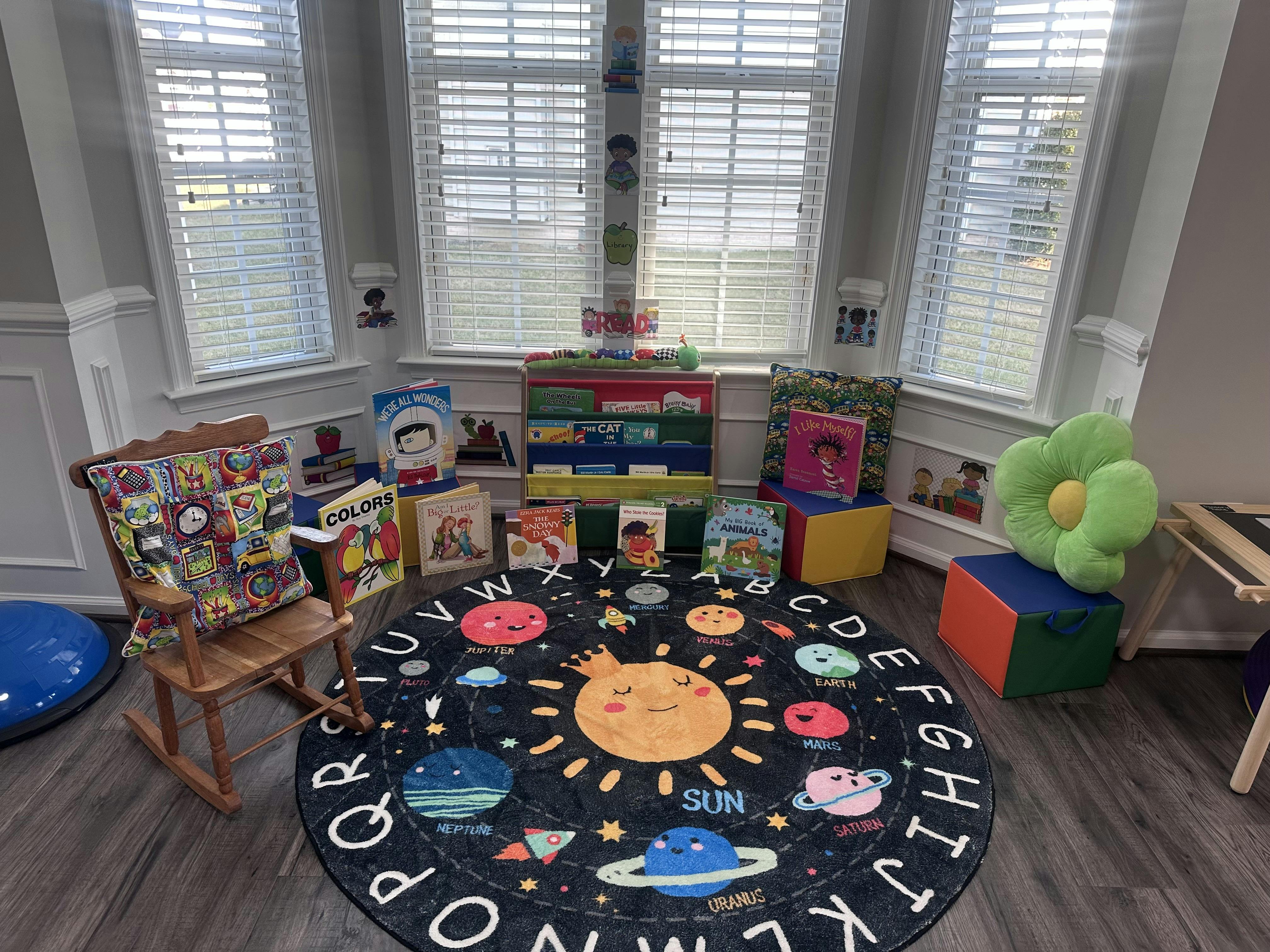 Reading nook in a children's classroom with books, a rocking chair, and a solar system rug