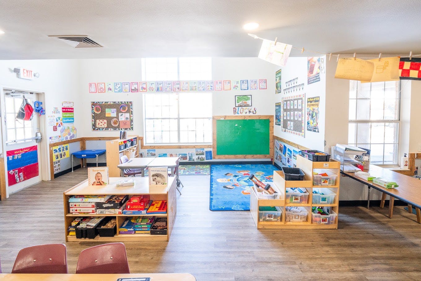 Classroom interior with tables, shelves of toys and books, and a play rug