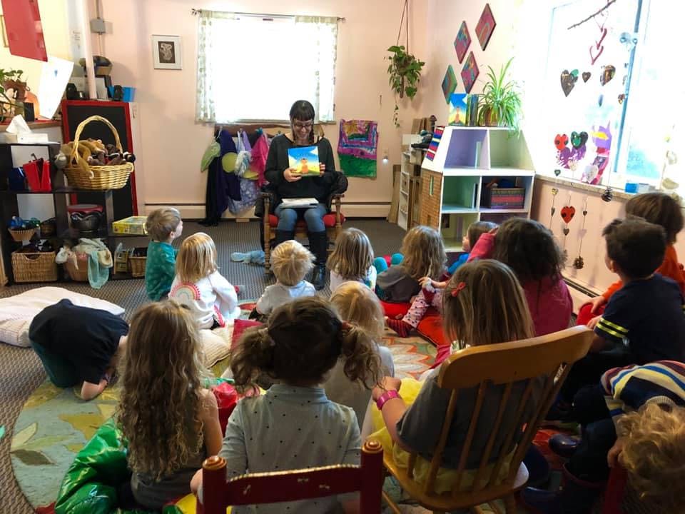 Person reading a book to a group of children in a classroom