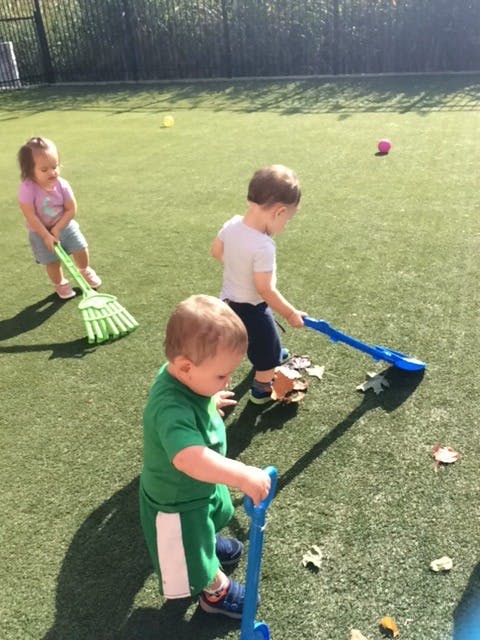 Three children playing with toy rakes on a grassy field