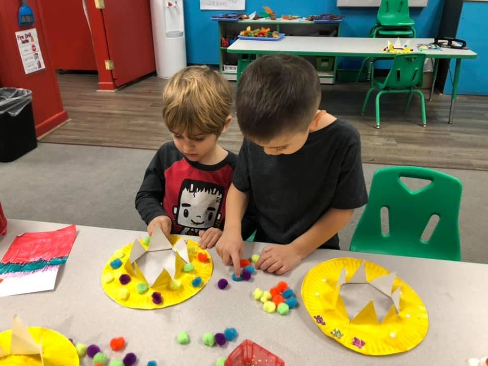 Two children making crafts with pom-poms in a classroom