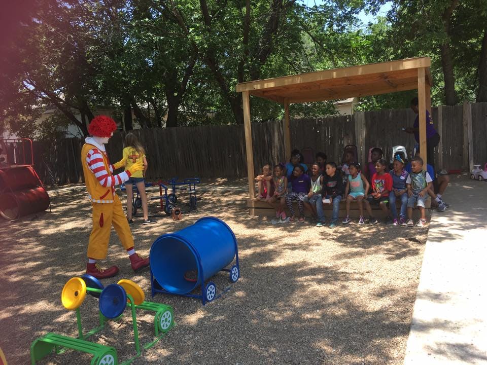 Person in clown costume with children sitting under a shelter