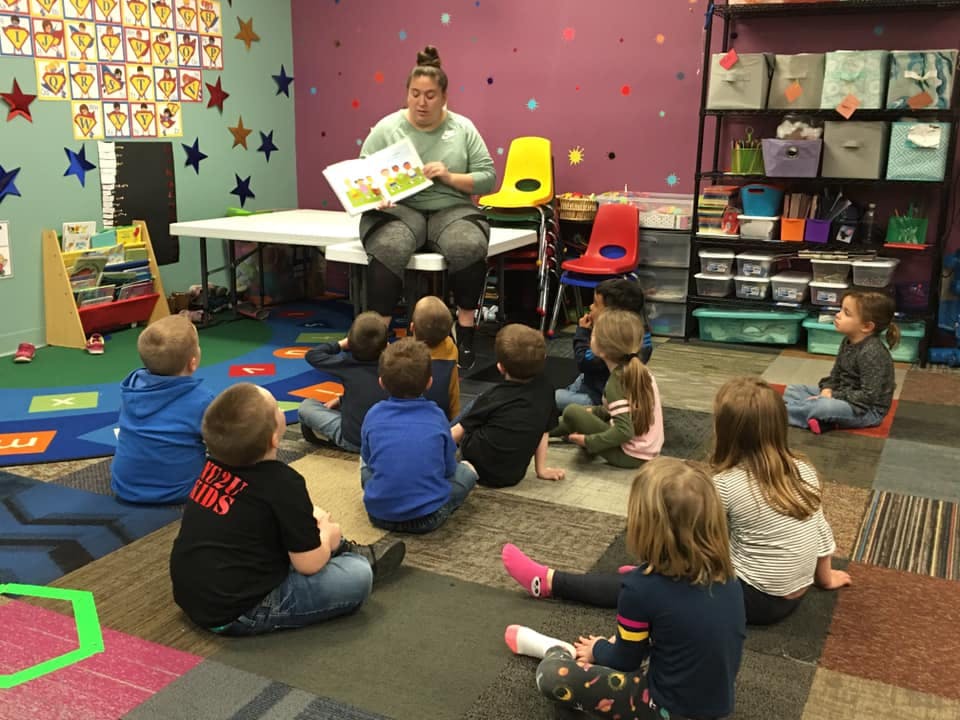 Adult reading a book to a group of children in a classroom