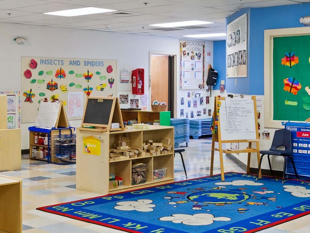 Classroom with children's art on walls, easels, and a blue rug with a world map