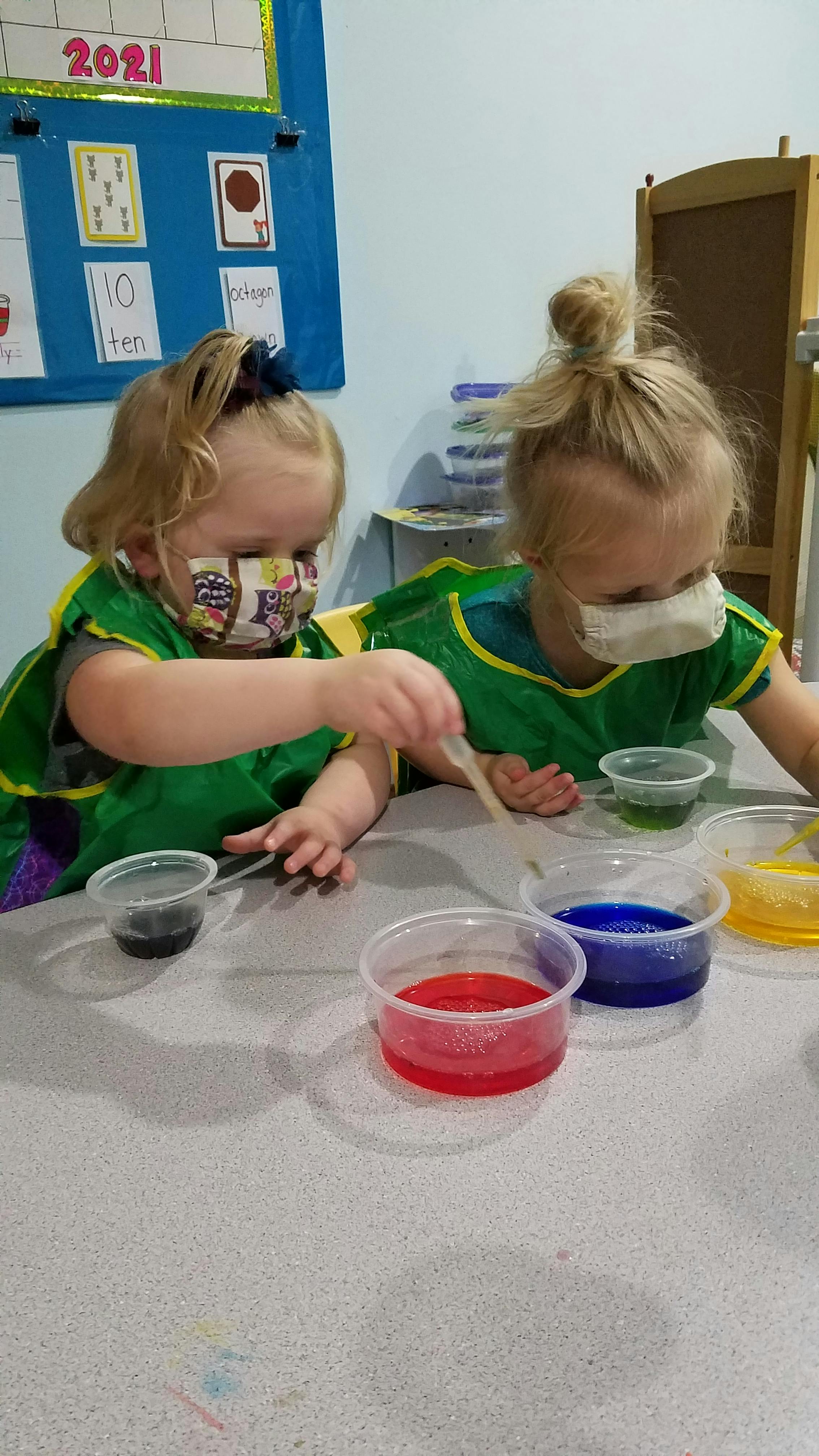 Two children in smocks using droppers with colorful liquids