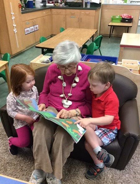Person reading a book to two children in a classroom