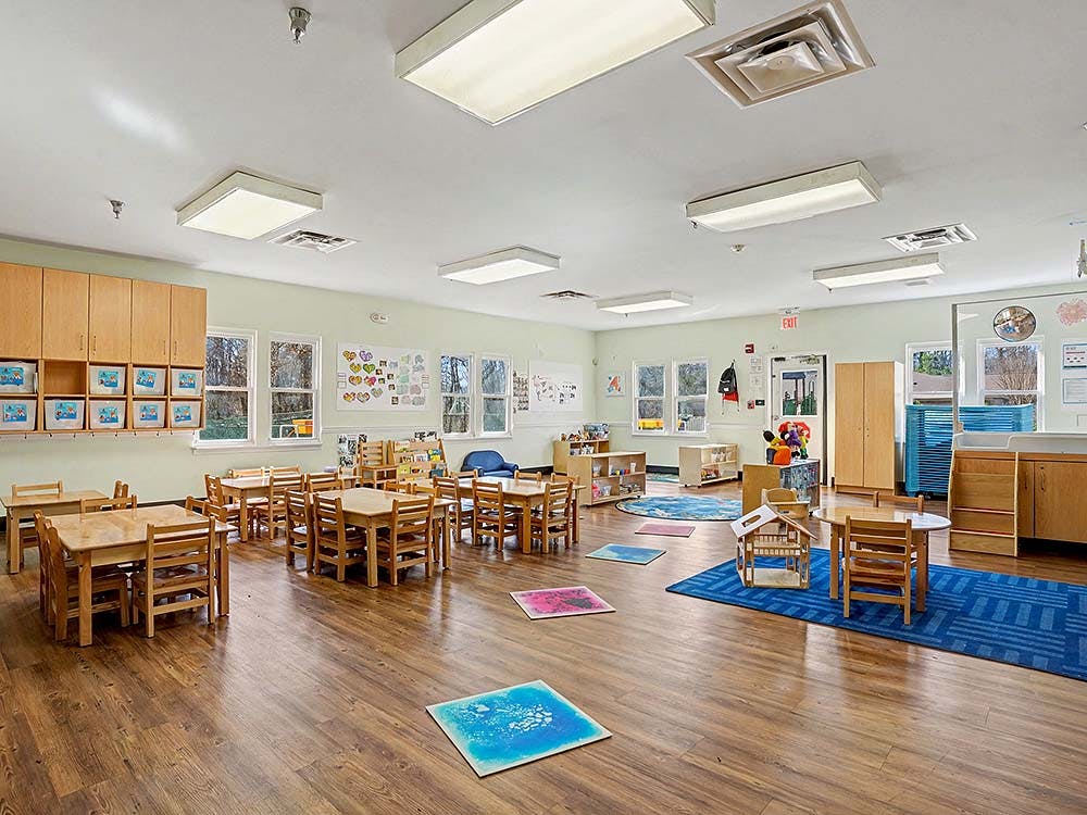 Empty classroom with small wooden tables and chairs, and bright floor mats