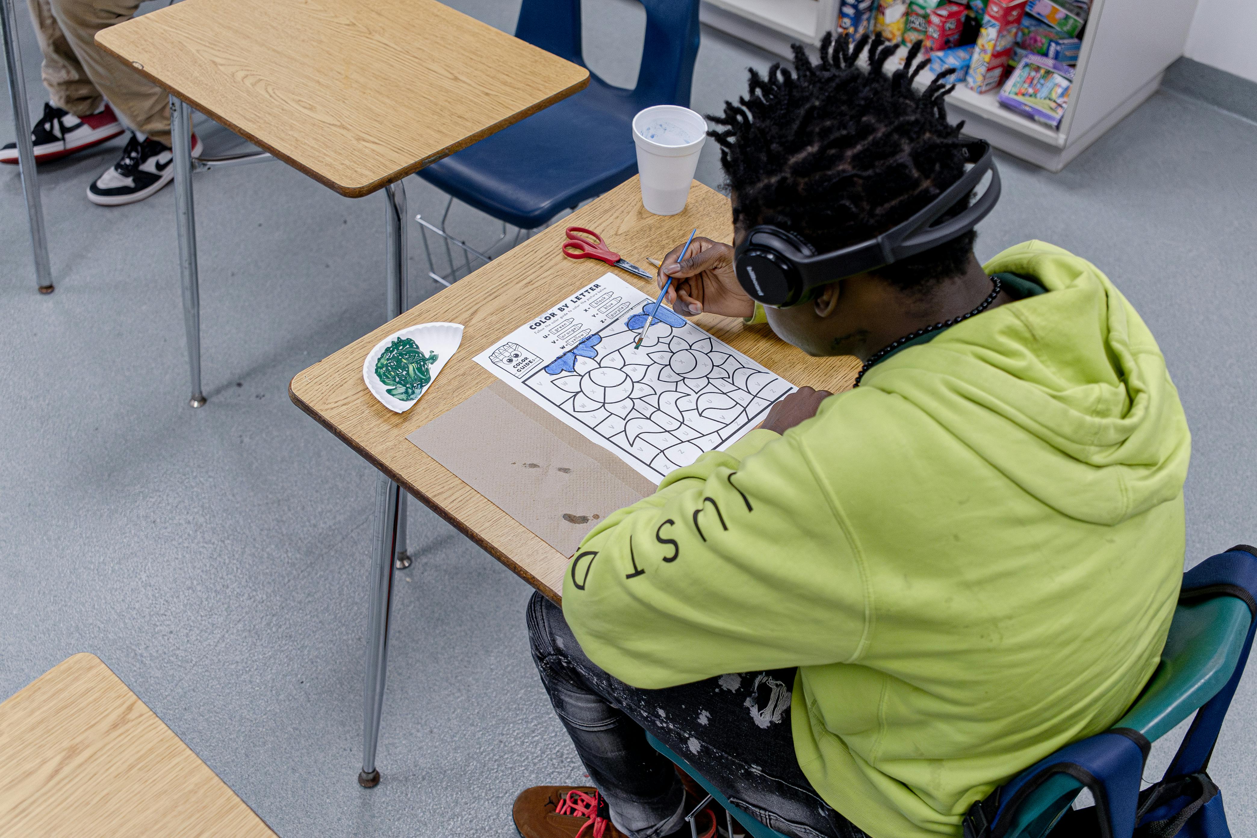Person wearing headphones painting a color by letter worksheet at a desk