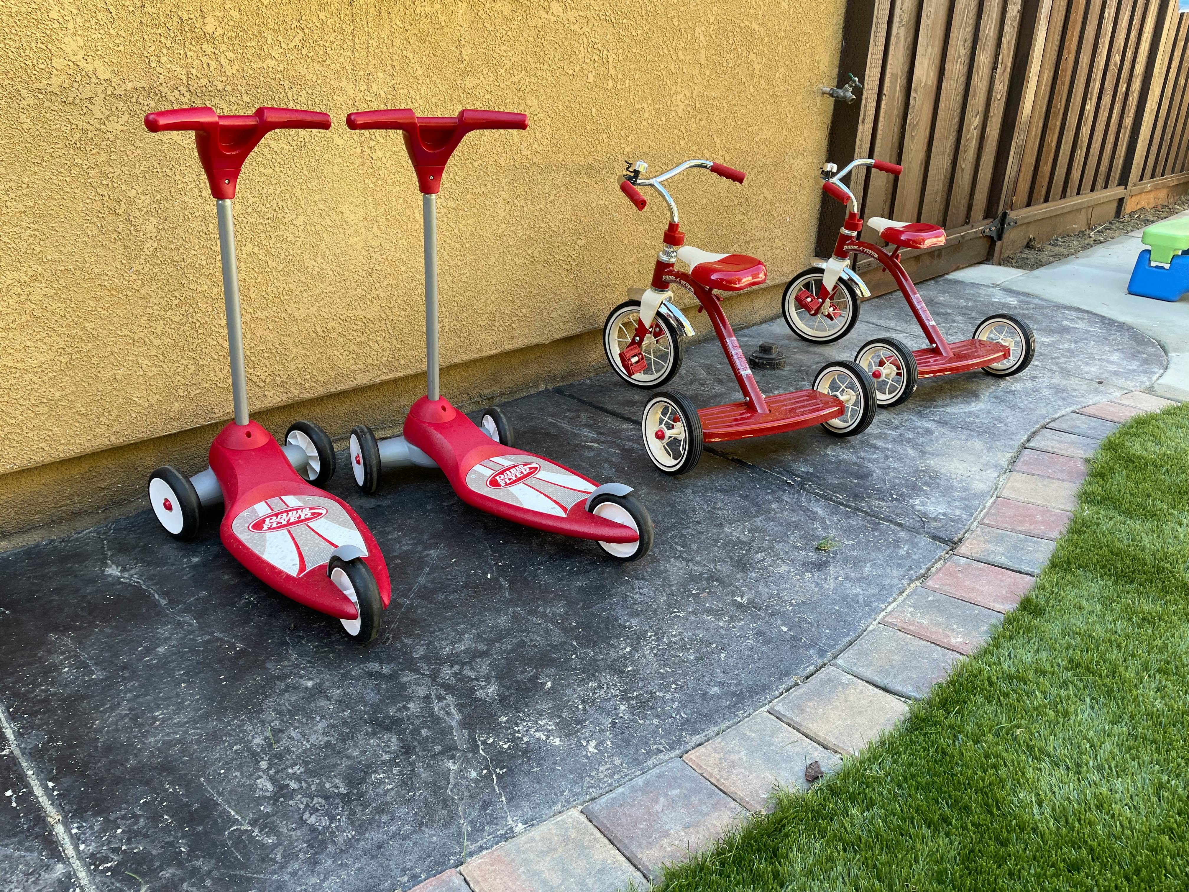 Two red scooters and two red tricycles on a patio