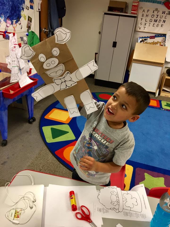 Child holding up a paper bag puppet with paper cutouts of a pig's face and body