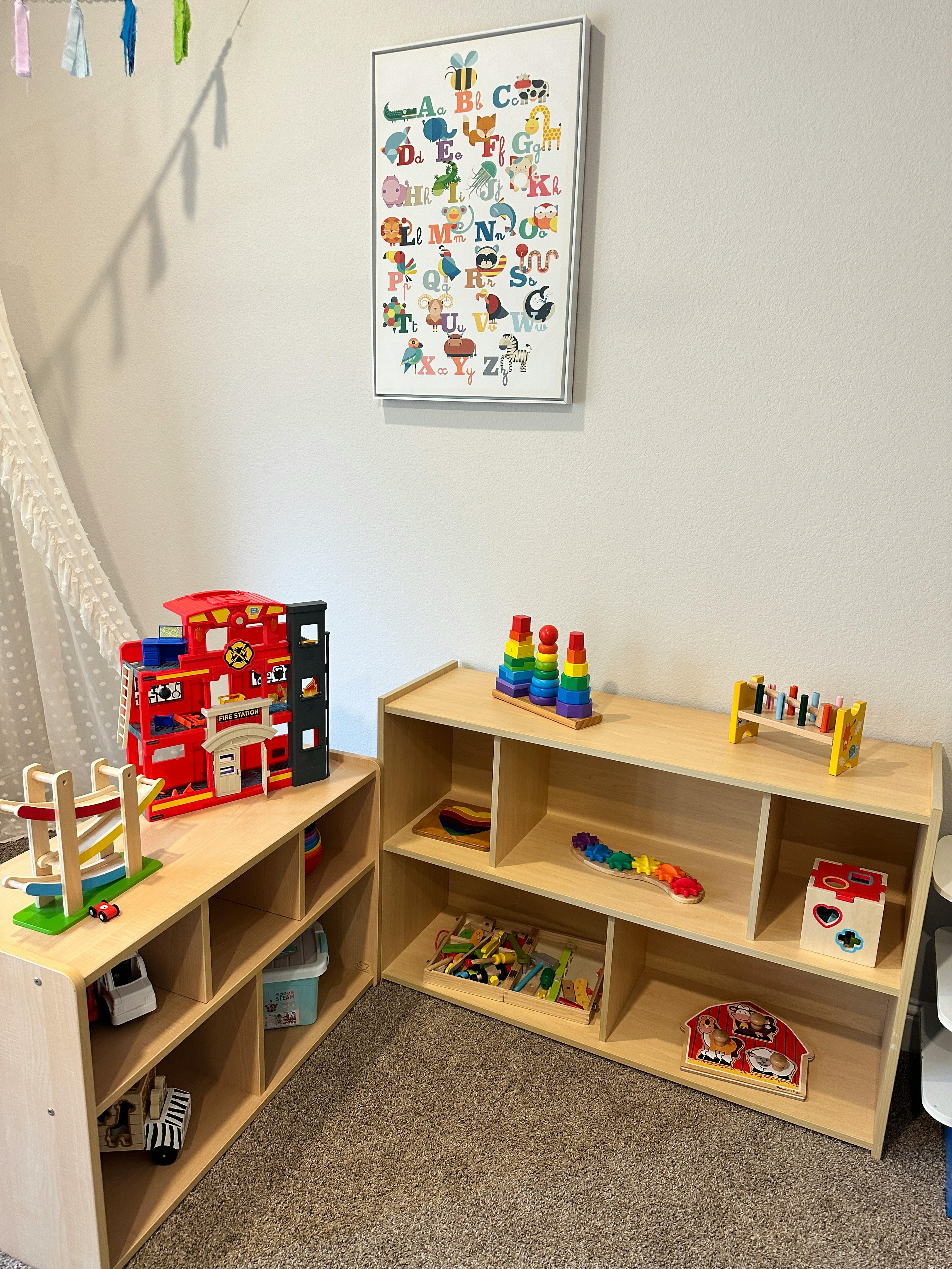 Playroom with wooden shelves holding toys and an alphabet poster on the wall