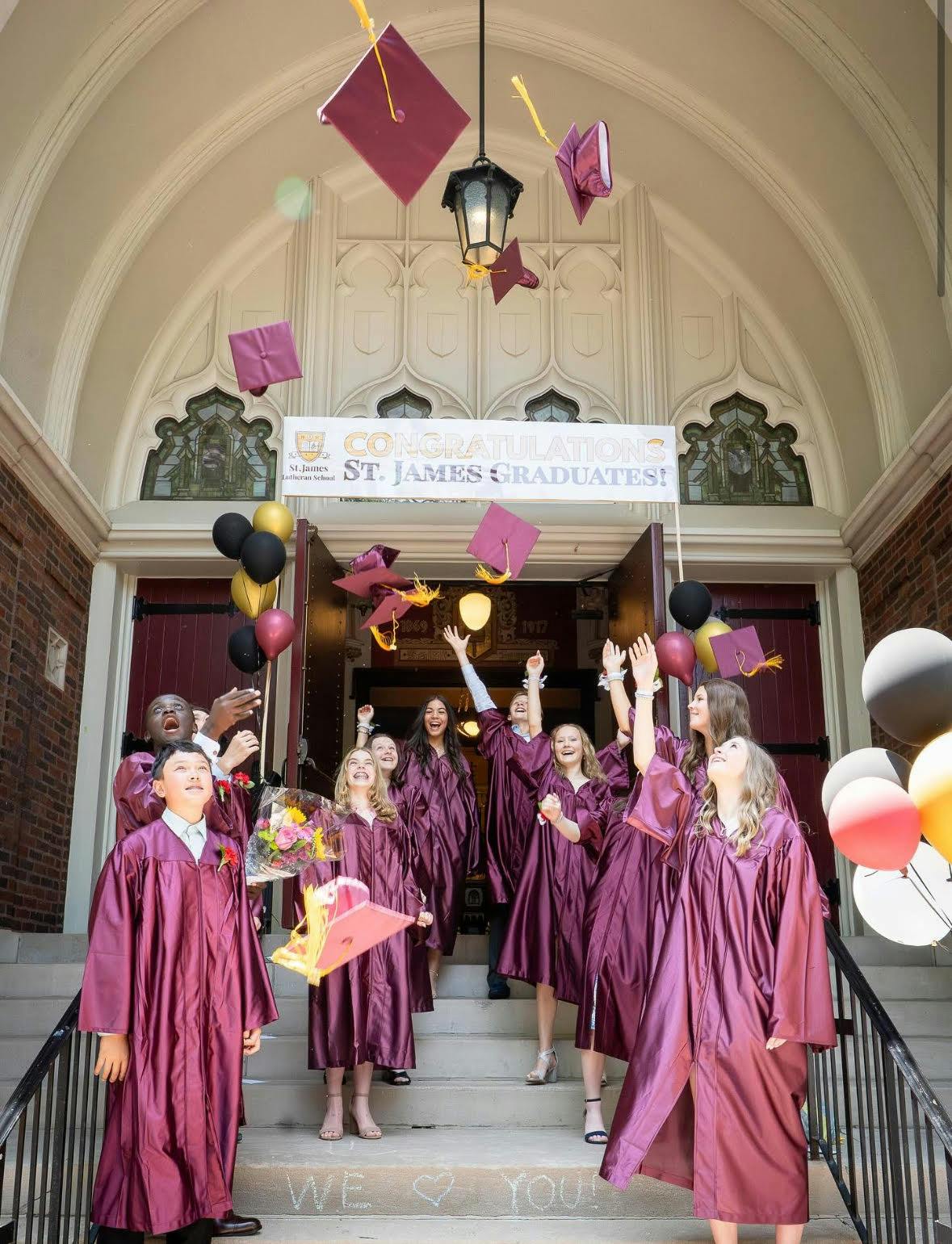 Graduates in maroon gowns throwing caps in the air outside a building