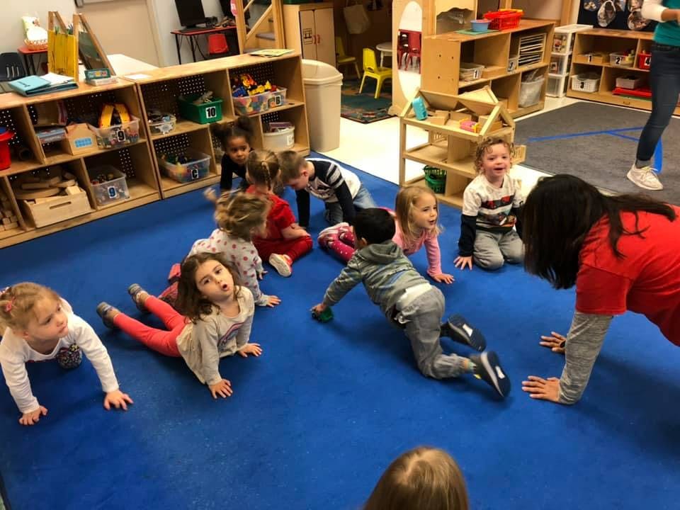 Children and an adult on hands and knees on a blue mat in a classroom
