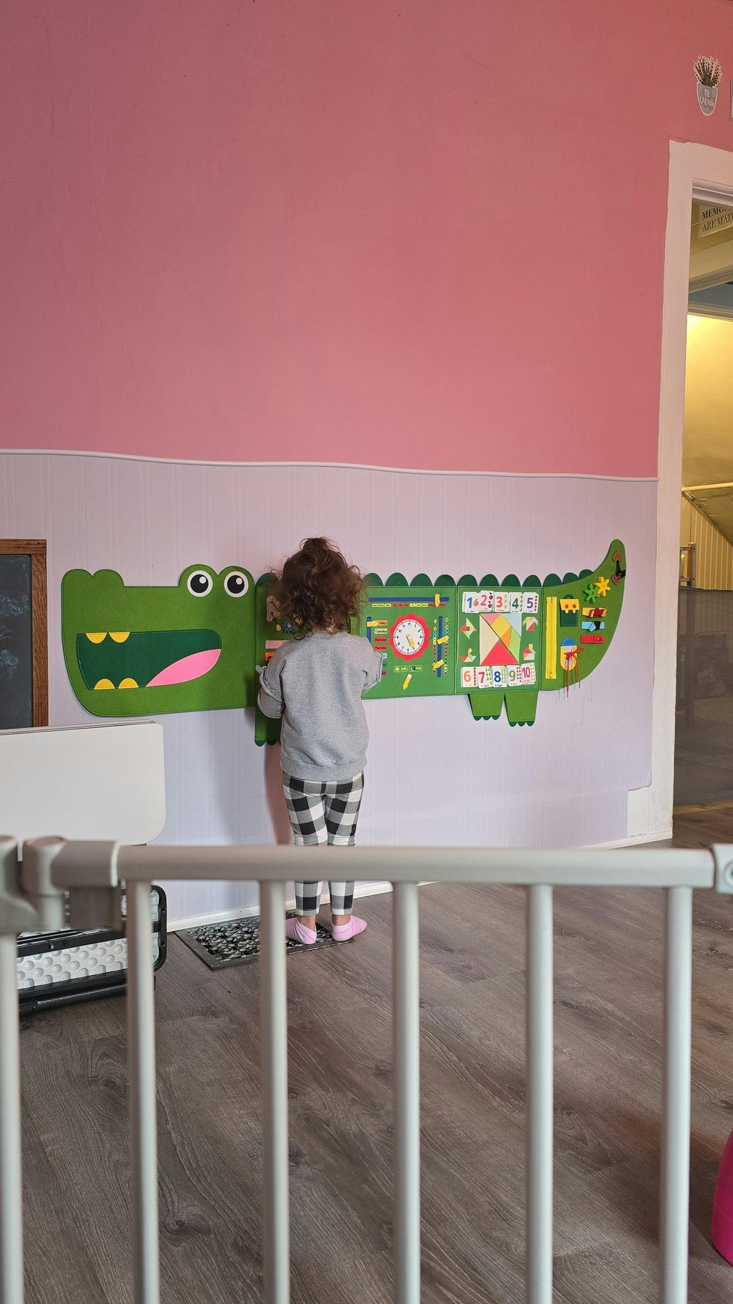 Child interacting with a large green alligator-shaped activity board on a wall