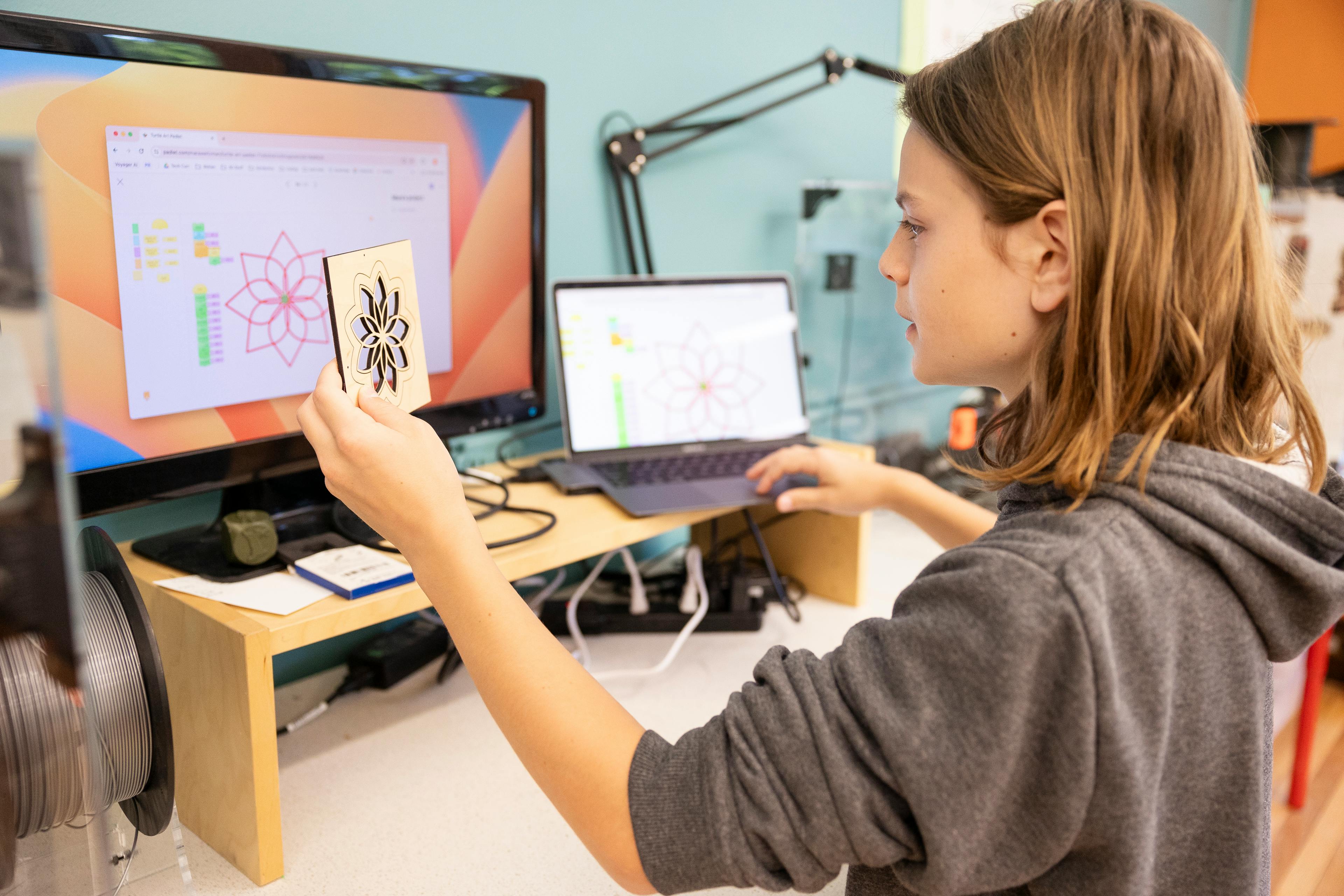 Teen holding a small wooden cutout while looking at a computer screen